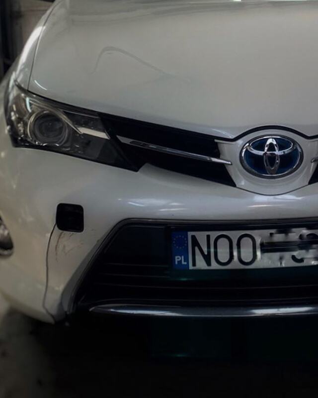 Biała Toyota Auris przed naprawą: pęknięty i porysowany przedni zderzak