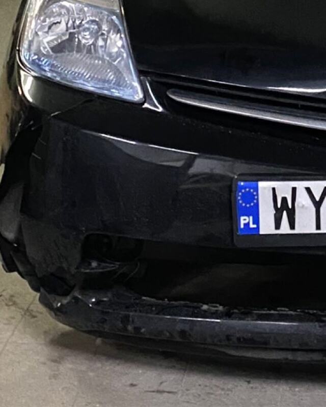 Czarna Toyota Prius przed naprawą: rozdarty róg i dolna krawędź przedniego zderzaka